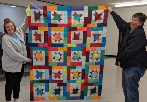Angi, left, with help from Brenda, holds up her completed quilt top.